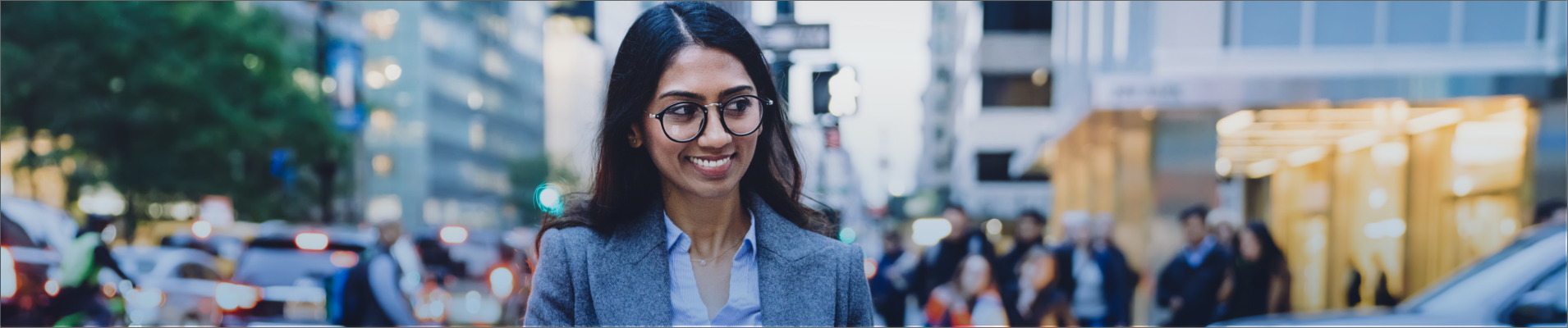 Woman with dark hair and glasses wearing gray blazer waking outdoors in New York City