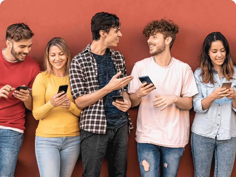 Group of people leaning against a wall looking at phones