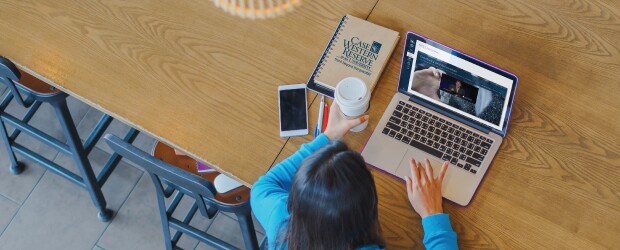 student with coffee watching a instructor video with a Case Western book