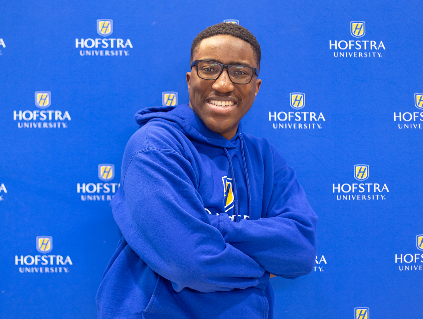Hofstra student posing with a Hofstra sweatshirt on in front of a Hofstra backdrop