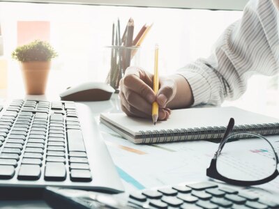 Financial analyst reviews financial report while taking notes on notepad.