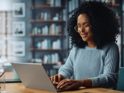 Smiling female of color sitting at a desk in a her home using a laptop