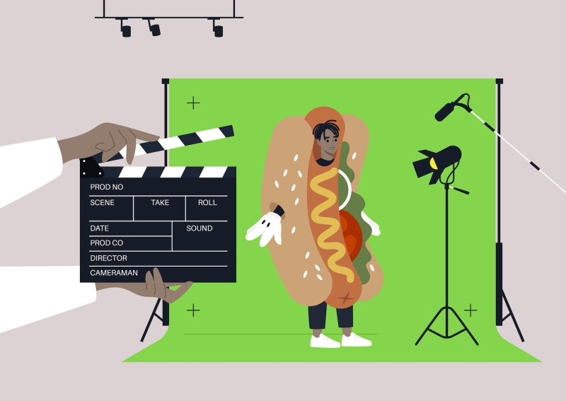 Man wearing hot dog suit filming in front of green screen.