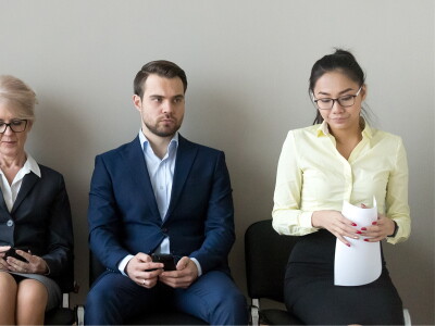 Row of three men and two women seated against a wall. They appear to be waiting for an interview.
