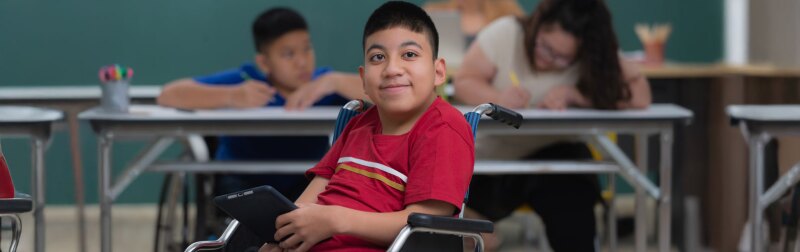 Portrait of young handicapped kid boy sitting on wheelchair and looking to camera with happiness eyes.