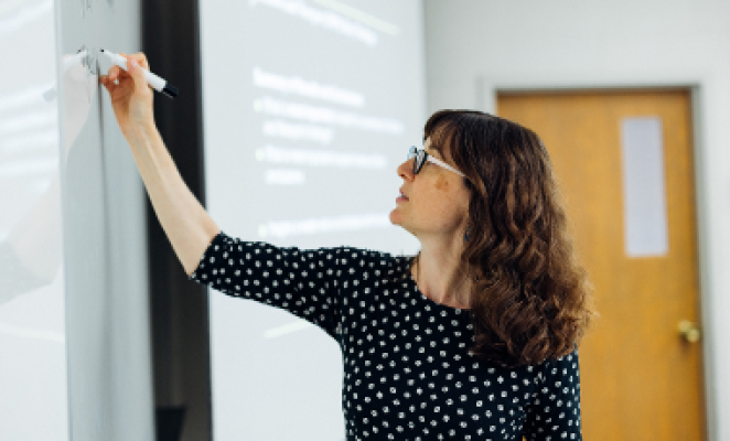 woman with glasses writing on a whiteboard