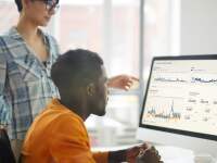Seated man and standing woman looking at graphs on desktop screen