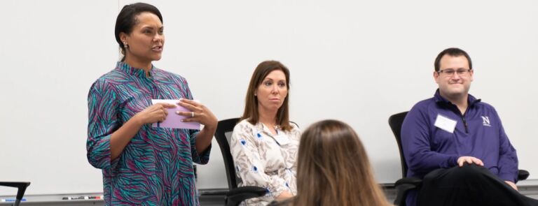 Woman standing speaking to a a room of seated individuals