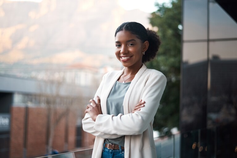 Woman standing on outdoor balcony in blazer crossing arms and smiling