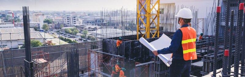 Civil engineer inspecting and working outdoors building side with blueprints.