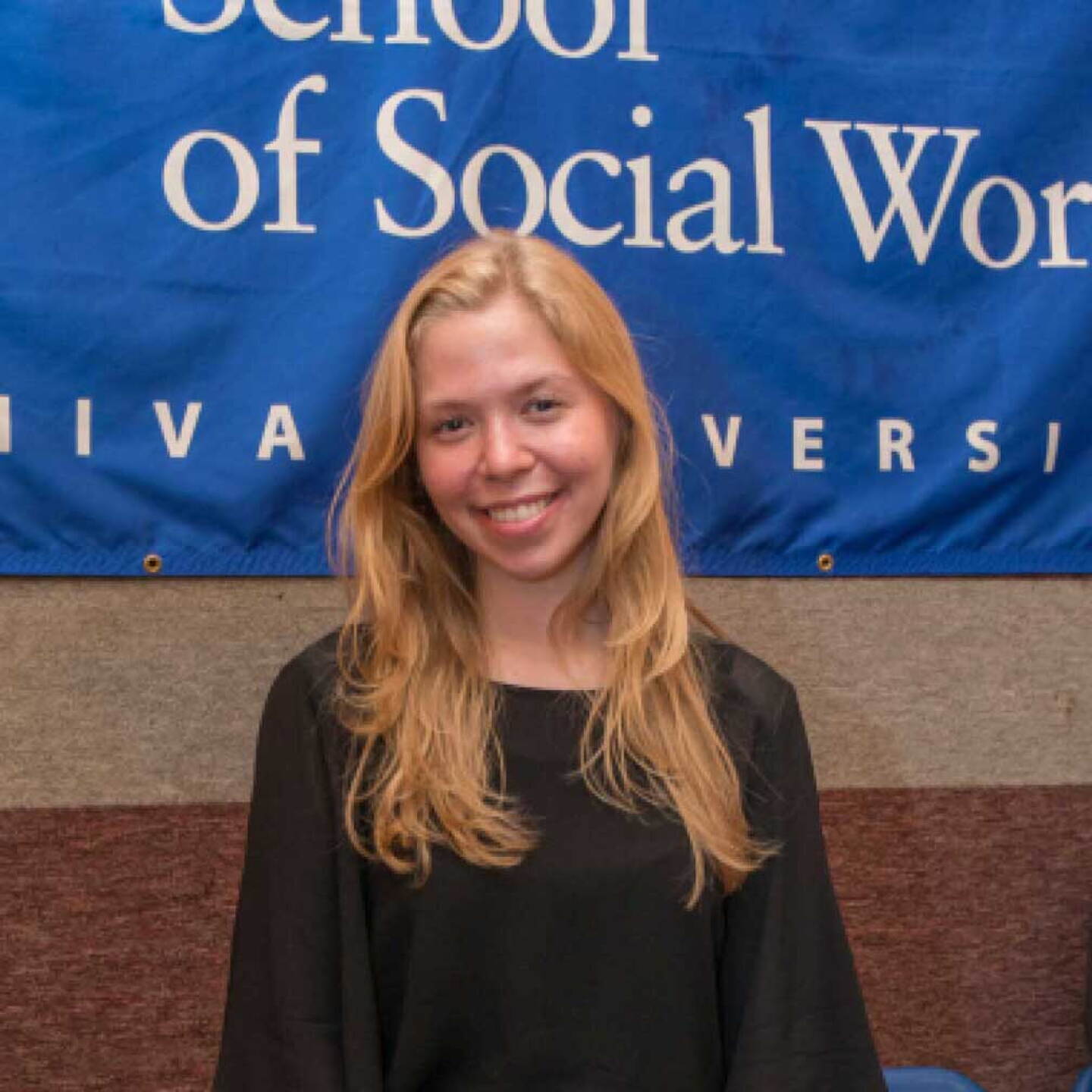 A female Yeshiva University student stands in front of a Wurzweiler backdrop.
