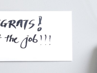 Sticky note on a desk next to mouse reads "congrats! you got the job!"