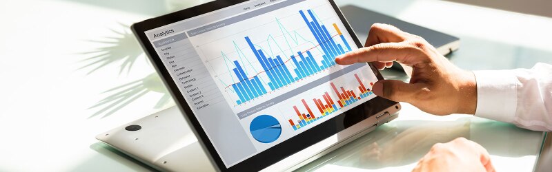 Close-up of a businessman's hand analyzing graphs on laptop at workplace.