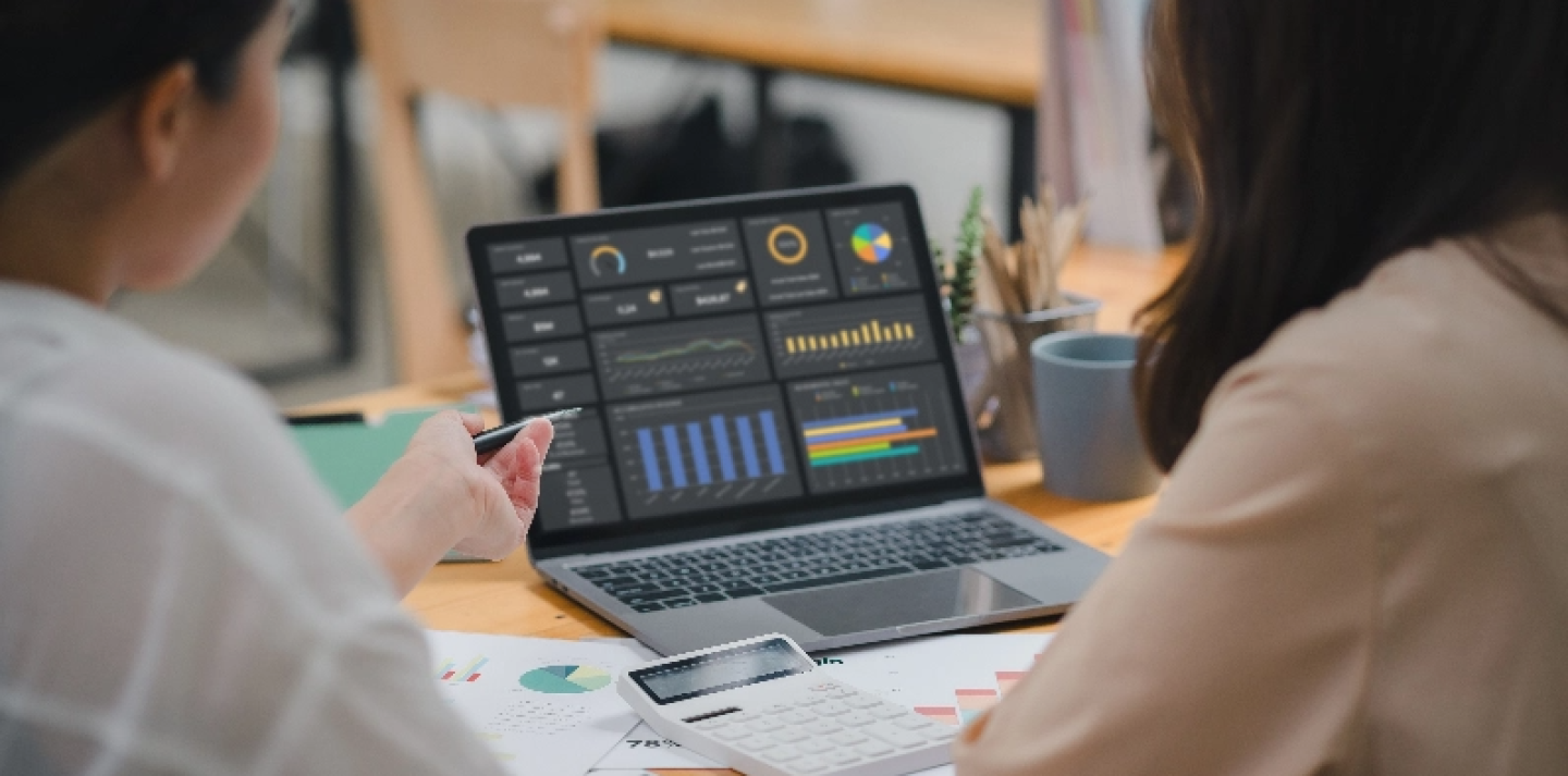 Two woman seated at desk in front of laptop displaying graphs