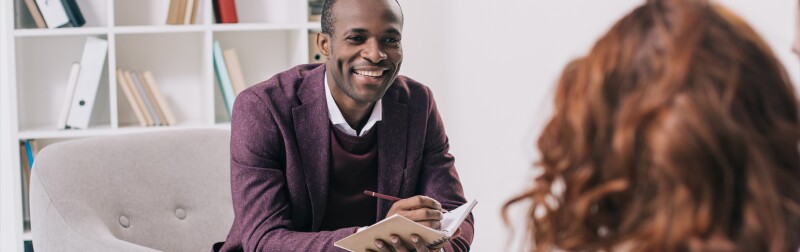Smiling african american male counselor talking to young female.