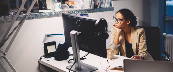 Woman in glasses seated at office desk looking at monitor