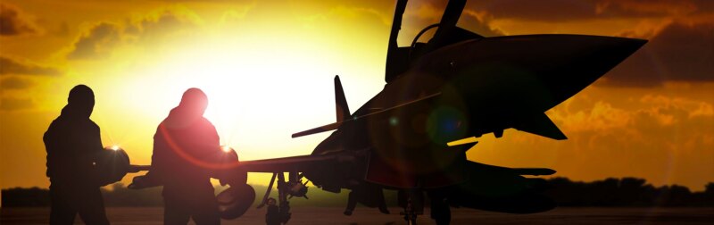 Silhouette of two military personnel working on a fighter jet at sunset, representing aviation maintenance and military operations