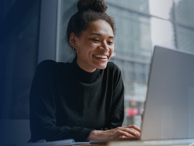A woman smiling while working on a laptop, with a rising graph overlay symbolizing the growth in social worker job opportunities.