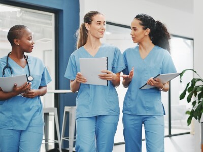 Three nurses walk through a clinic discussing a patient's case