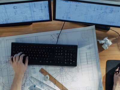 Someone working at a desk with blueprints and a computer.