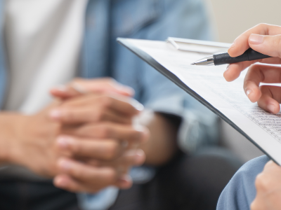 A close up of a mental health counselor taking notes during a session with a patient facing them