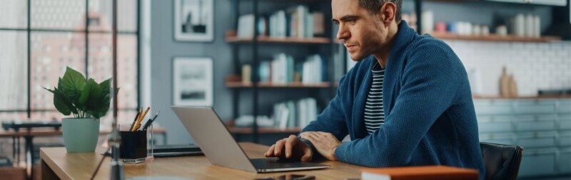 Male manager sits on a laptop at the kitchen table while communicating with team.