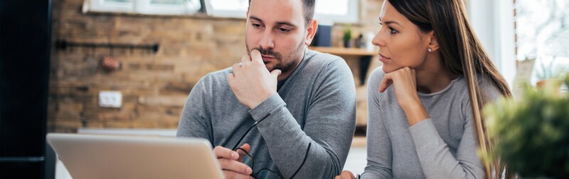 Couple managing finances in front of a laptop in their kitchen.