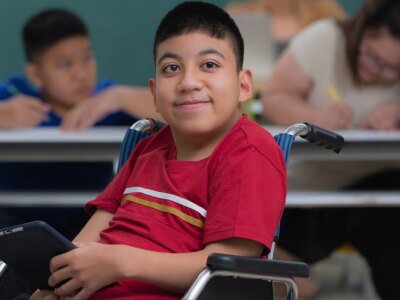 Portrait of young handicapped kid boy sitting on wheelchair and looking to camera with happiness eyes.
