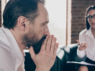 Man in a contemplative state during a counseling session, while the therapist engages in conversation