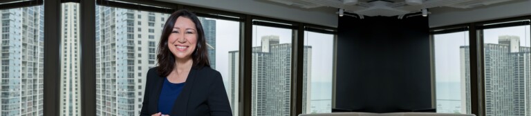 IMC alumni stands in office space while wearing a black blazer