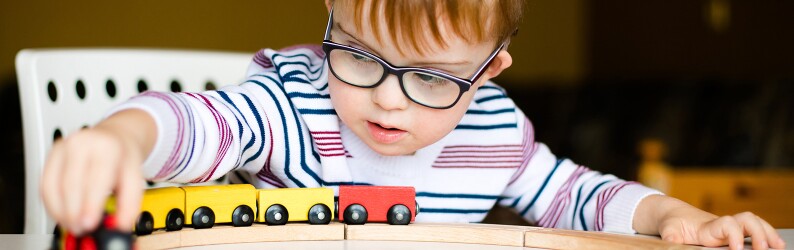 Little boy in the glasses playing with wooden trains