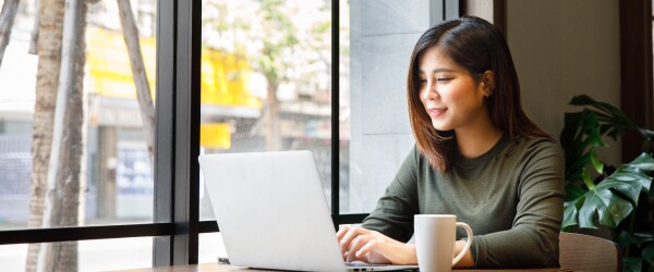 woman in green sweater sitting at laptop in front of window
