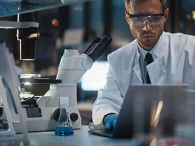 Scientists in a lab examine microscope samples and computer screens