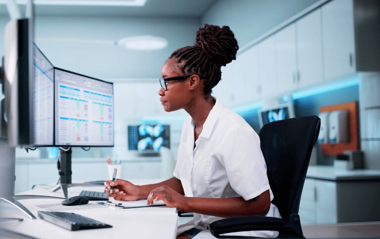 Woman in white outfit analyzing computer screen and making notes on clipboard