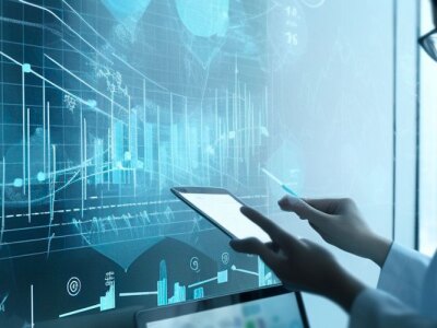 Female health professional holds a tablet while reviewing medical data on a wall monitor.