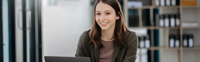 Woman seated in office working on laptop in front of shelf of books