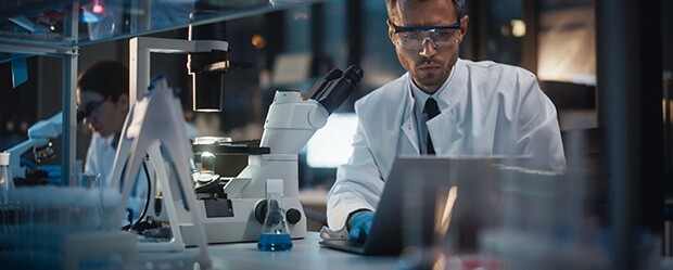 Scientists in a lab examine microscope samples and computer screens