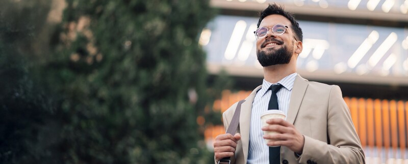 Smiling male attorney holding coffee walking outside office building