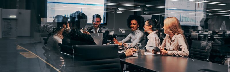 Group of business professionals gathered around meeting table for presentation.