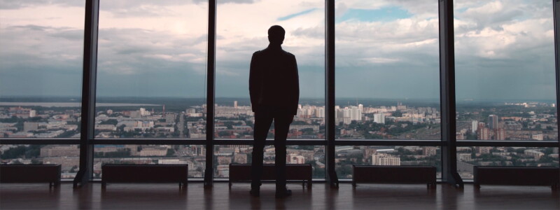 Man in suit standing in front of a window in a high-rise building.