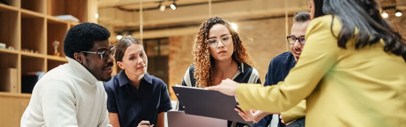 A diverse group of professionals engaged in a focused team meeting, reviewing a document together.