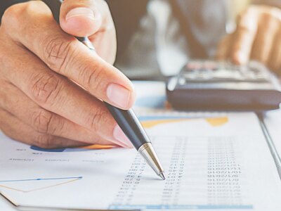 Business professional with pen in hand working with data sheet and calculator