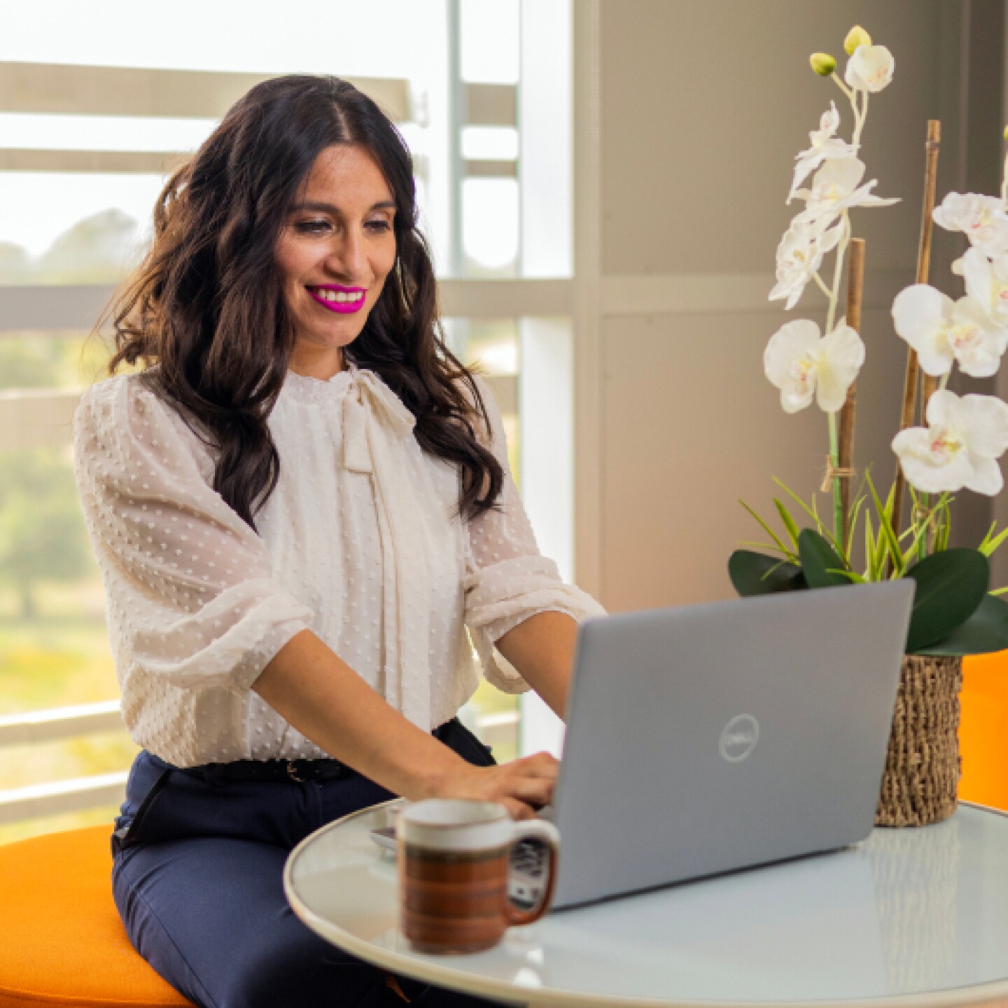 A female CSUMB student sitting in dining room with white lily flowers in background while typing on computer.
