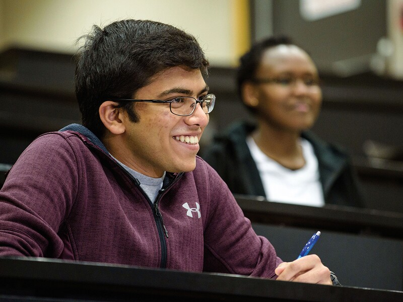 Smiling male student taking notes in class