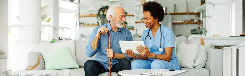 Elderly man holding cane speaking with Geriatric care nurse on couch
