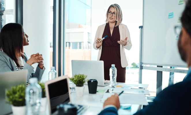 Woman at a whiteboard in front of a meeting room, leading a discussion