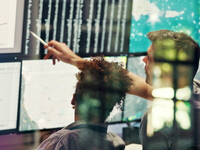 A man and a woman sit before a wall of screens, reviewing data.