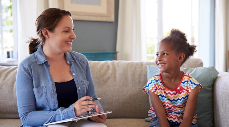 Young girl speaking on a couch with counselor holding a clipboard