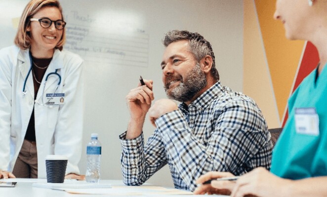 Female doctor, nurse and man seated together at table in front of whiteboard