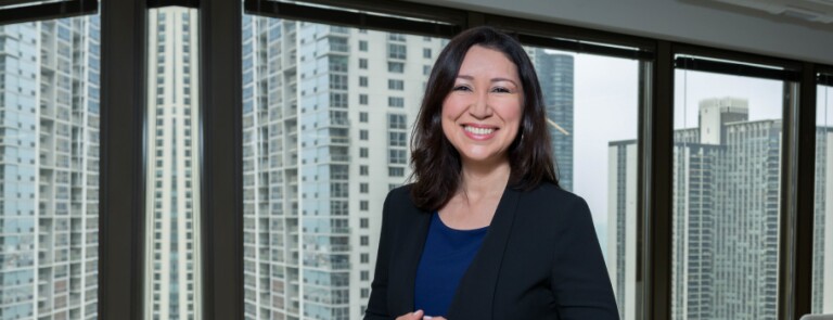 IMC alumni stands in office space while wearing a black blazer
